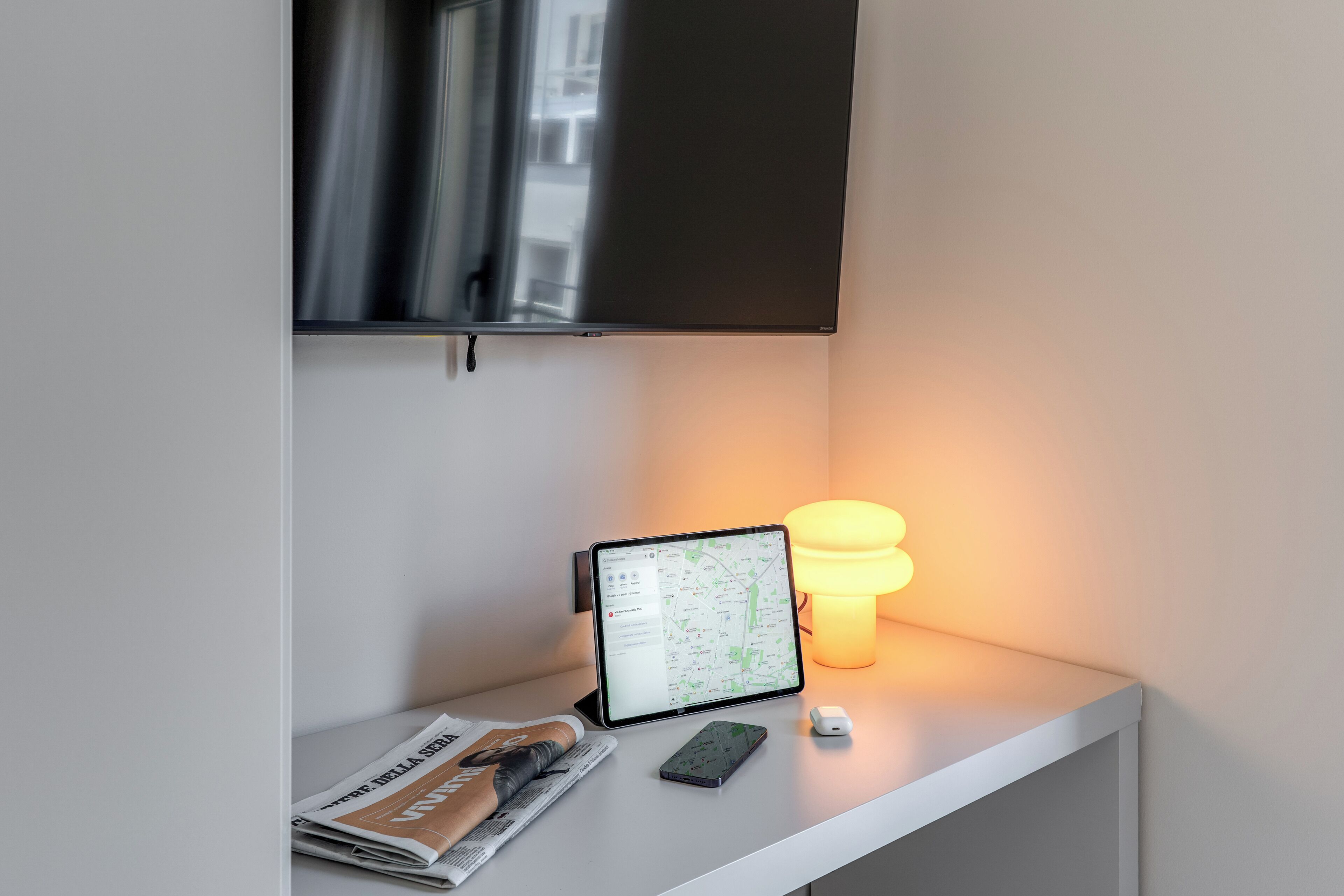 Uma mesa com um tablet mostrando um mapa, um smartphone, uma luminária e um jornal.