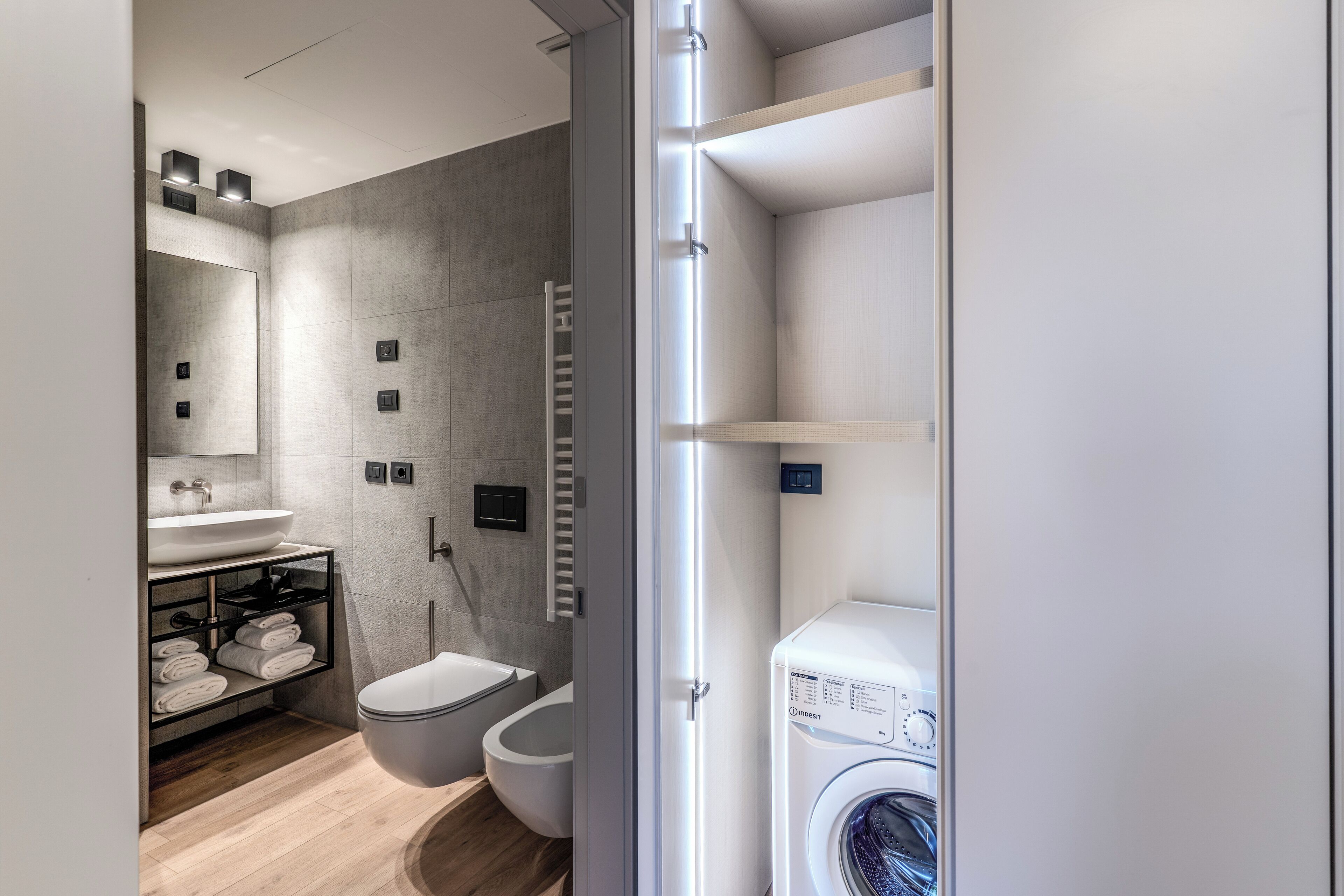 A modern bathroom with a built-in washing machine, a toilet, and a shelf with towels.
