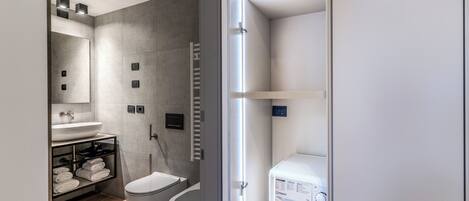 Un baño moderno con lavadora integrada, inodoro y estante con toallas.