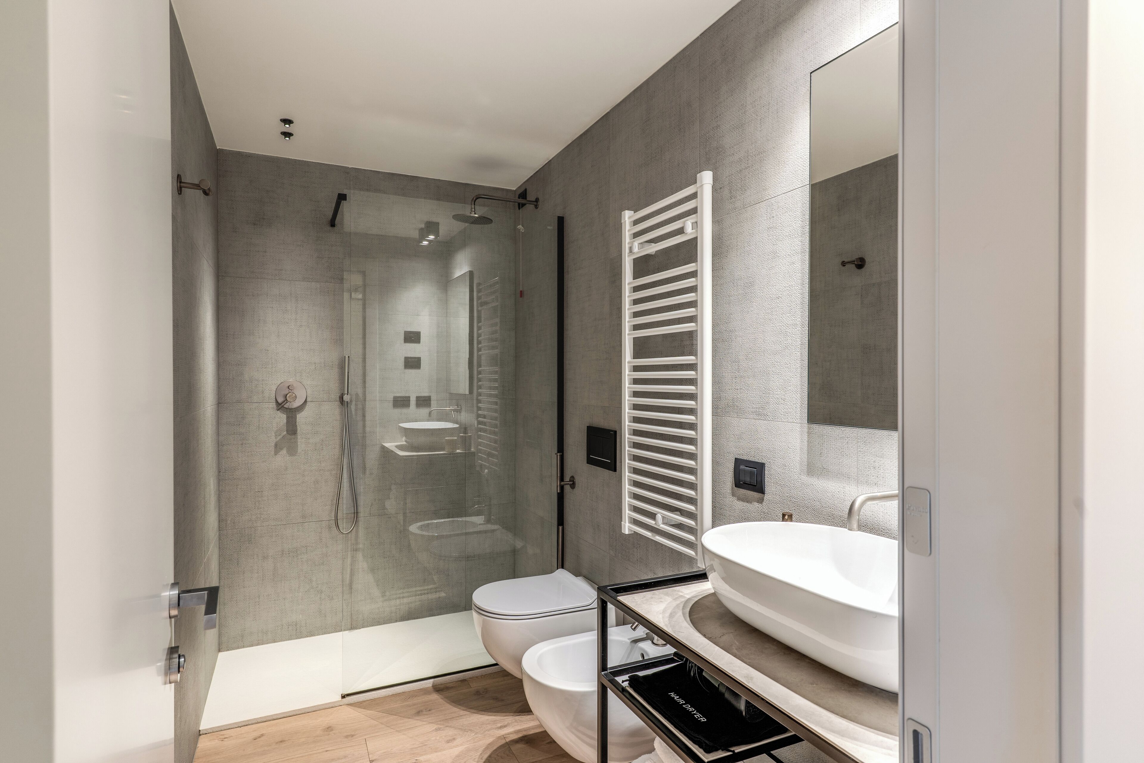 A modern bathroom with a glass-enclosed shower, a white toilet, a bathtub, and a large mirror.