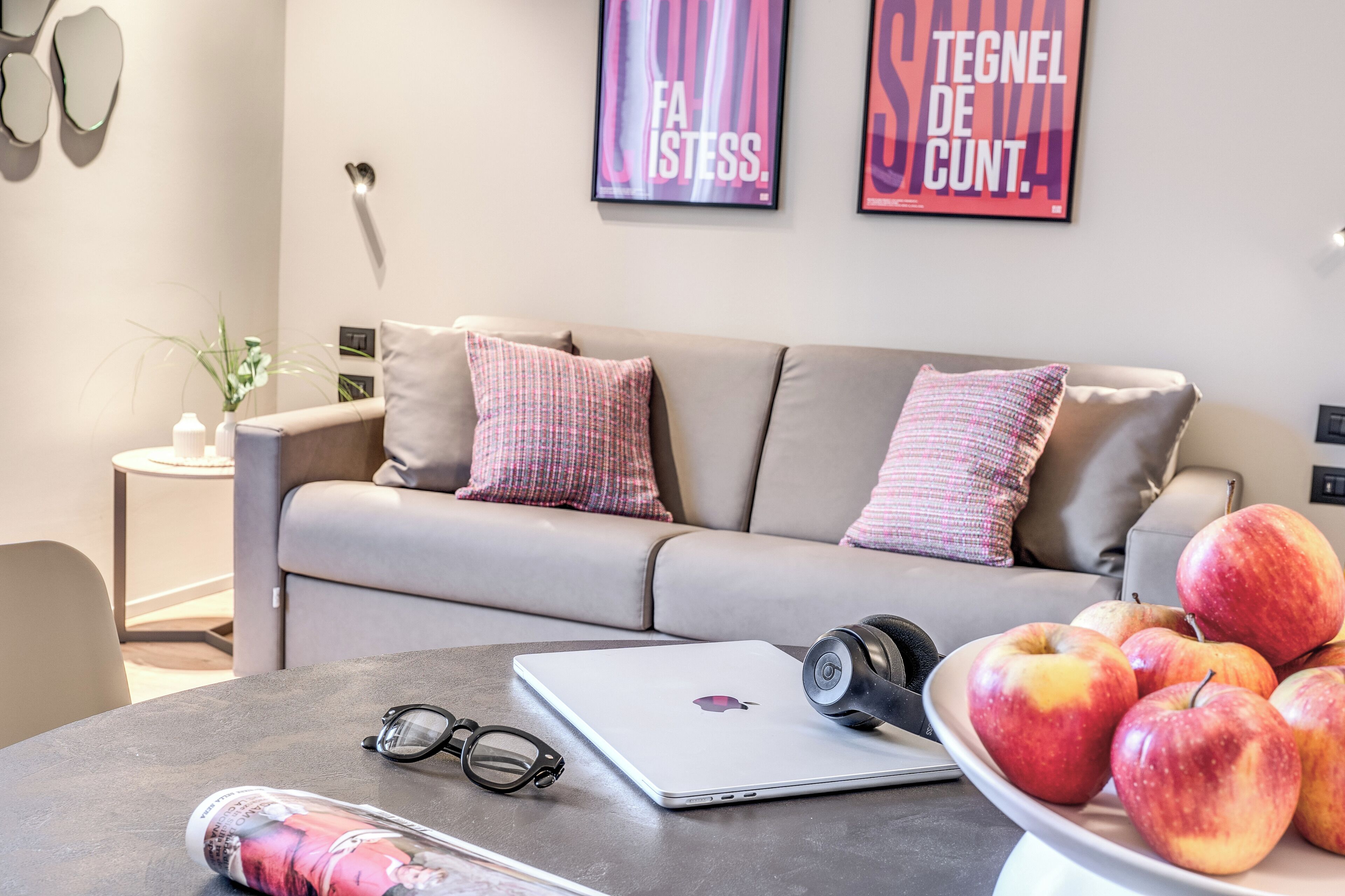 A modern living room with a sofa, a coffee table with a laptop, a bowl of apples, and a pair of glasses.