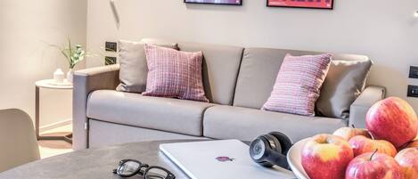 A modern living room with a sofa, a coffee table with a laptop, a bowl of apples, and a pair of glasses.