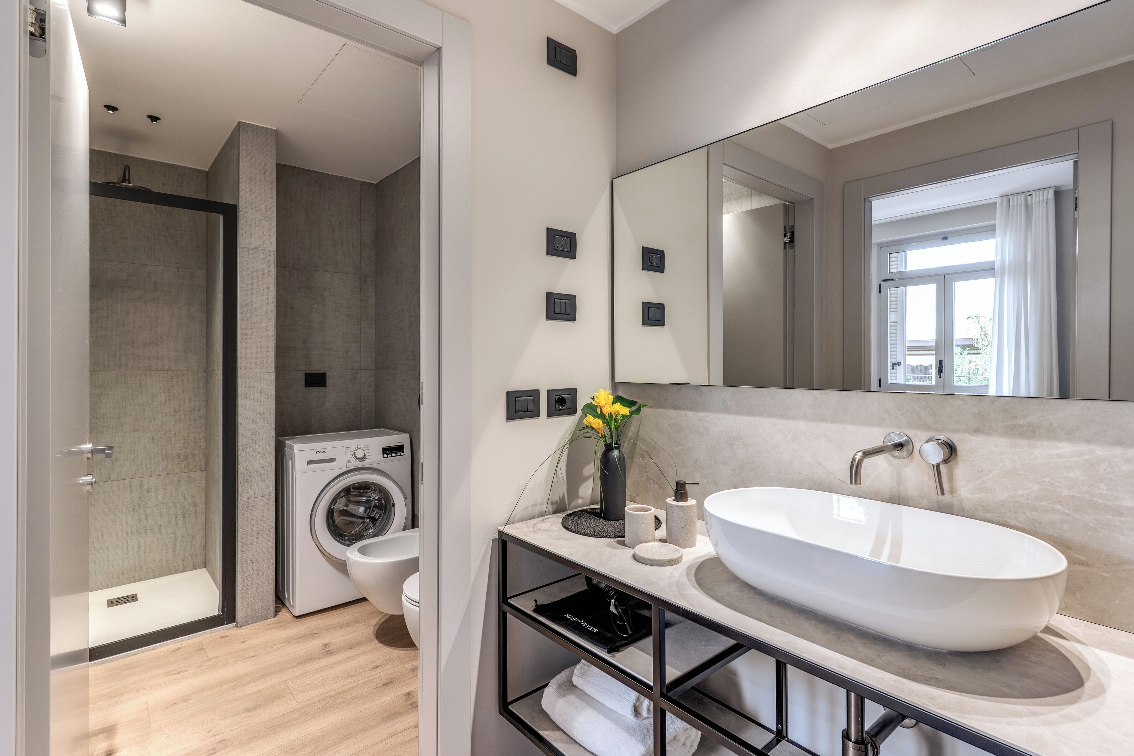 A modern bathroom with a large mirror, a sink, a shower, and a washing machine.