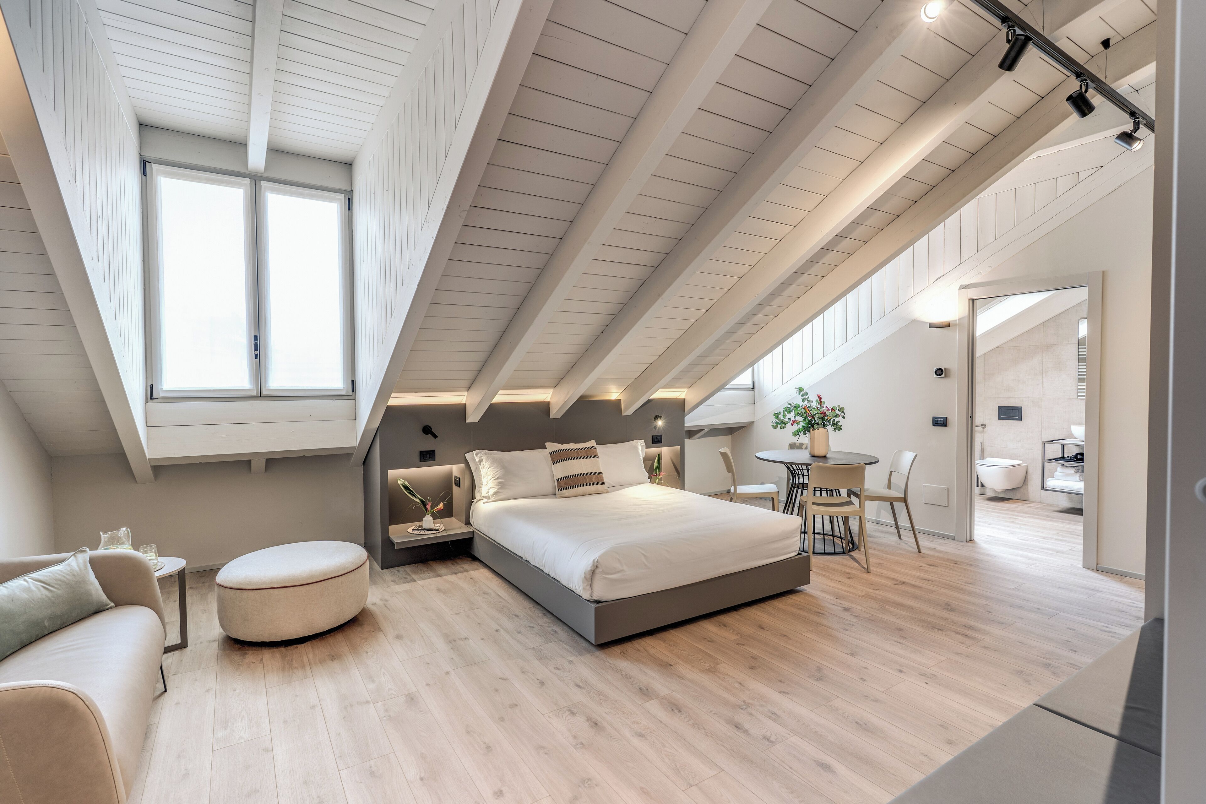 Ett modernt sovrum med ett tak i loftstil, en stor säng, en rund sittpuff och en liten matplats.