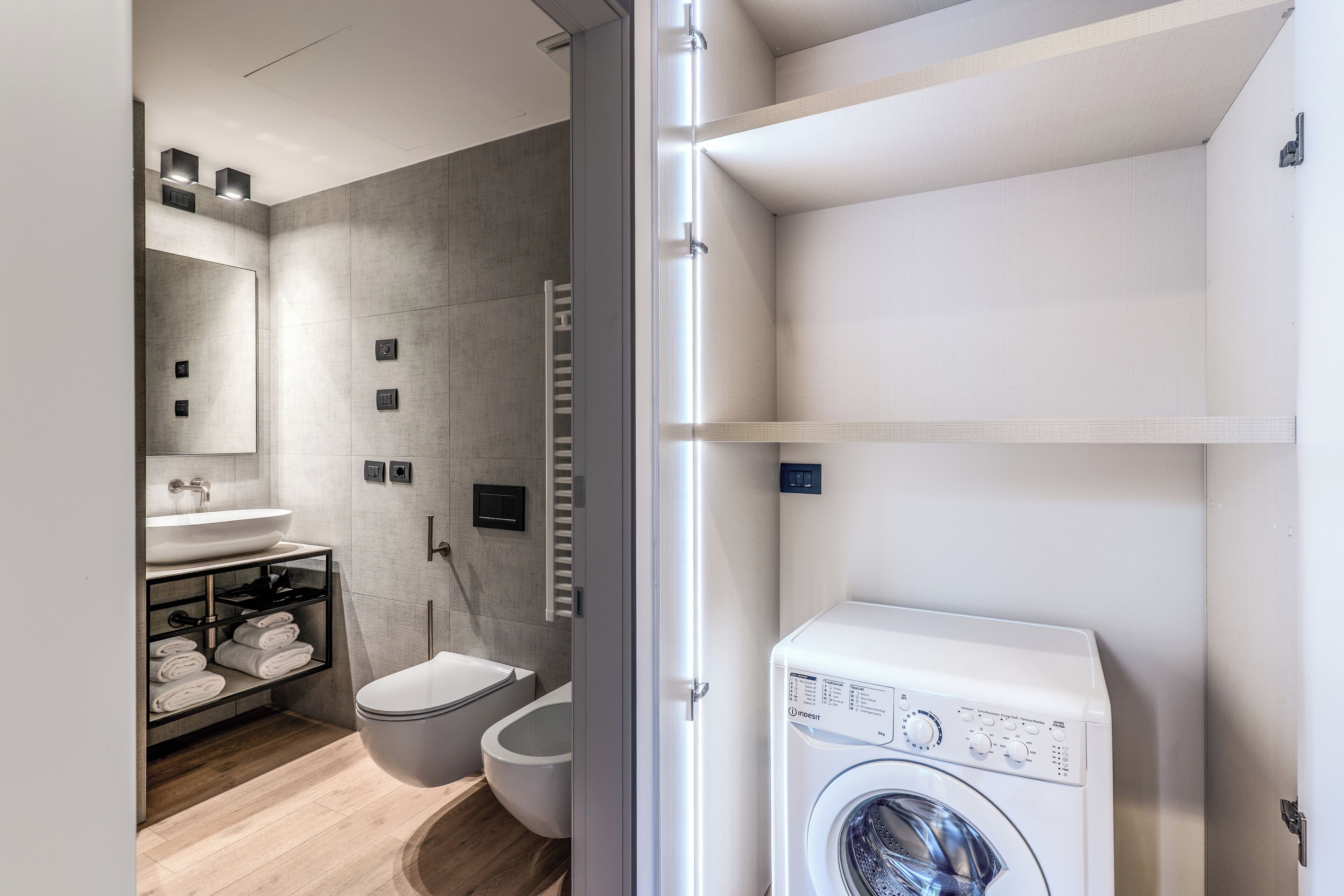 A modern bathroom with a built-in washing machine, a toilet, and a sink with a towel rack.