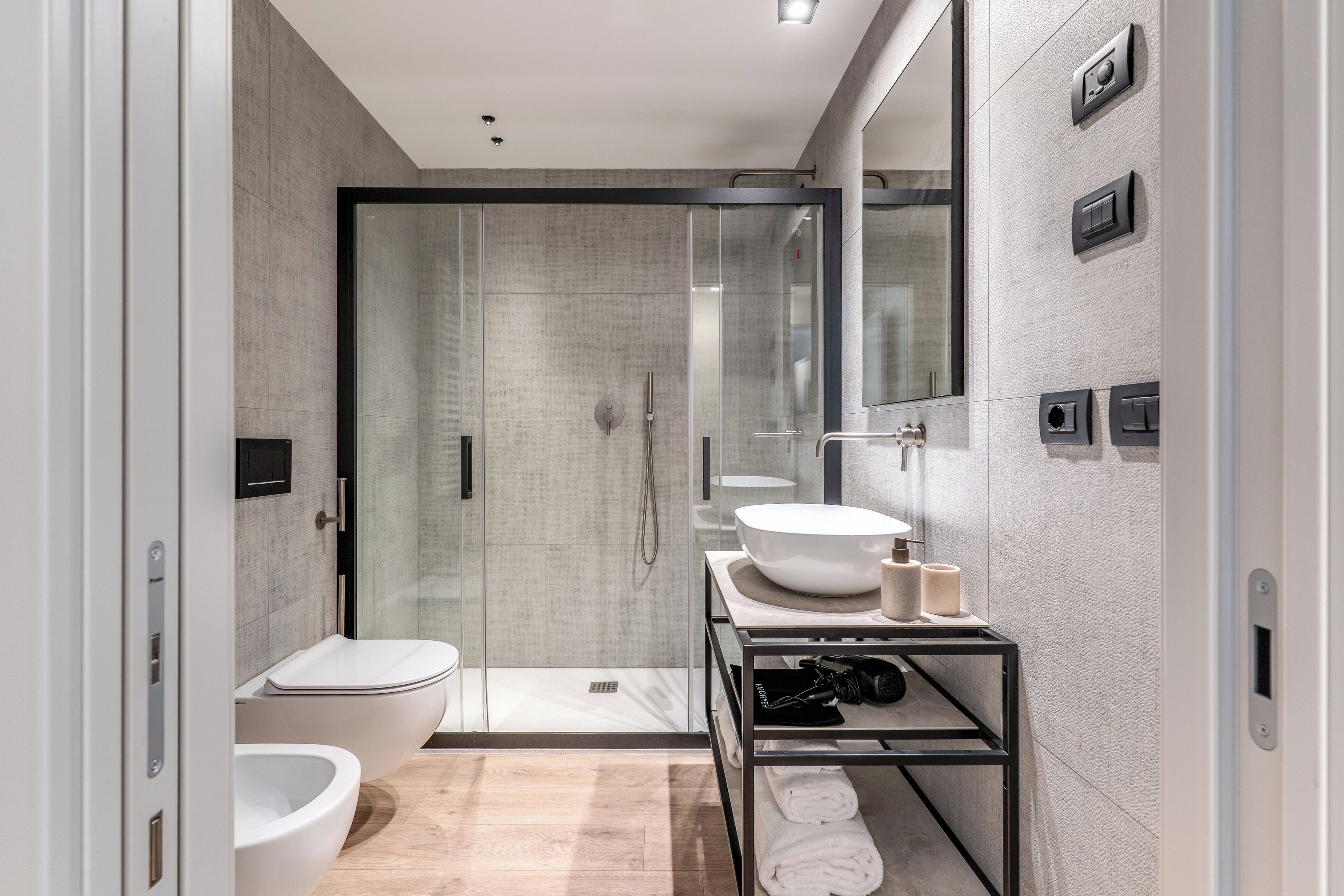A modern bathroom with a glass shower enclosure, a white sink, and a towel rack.