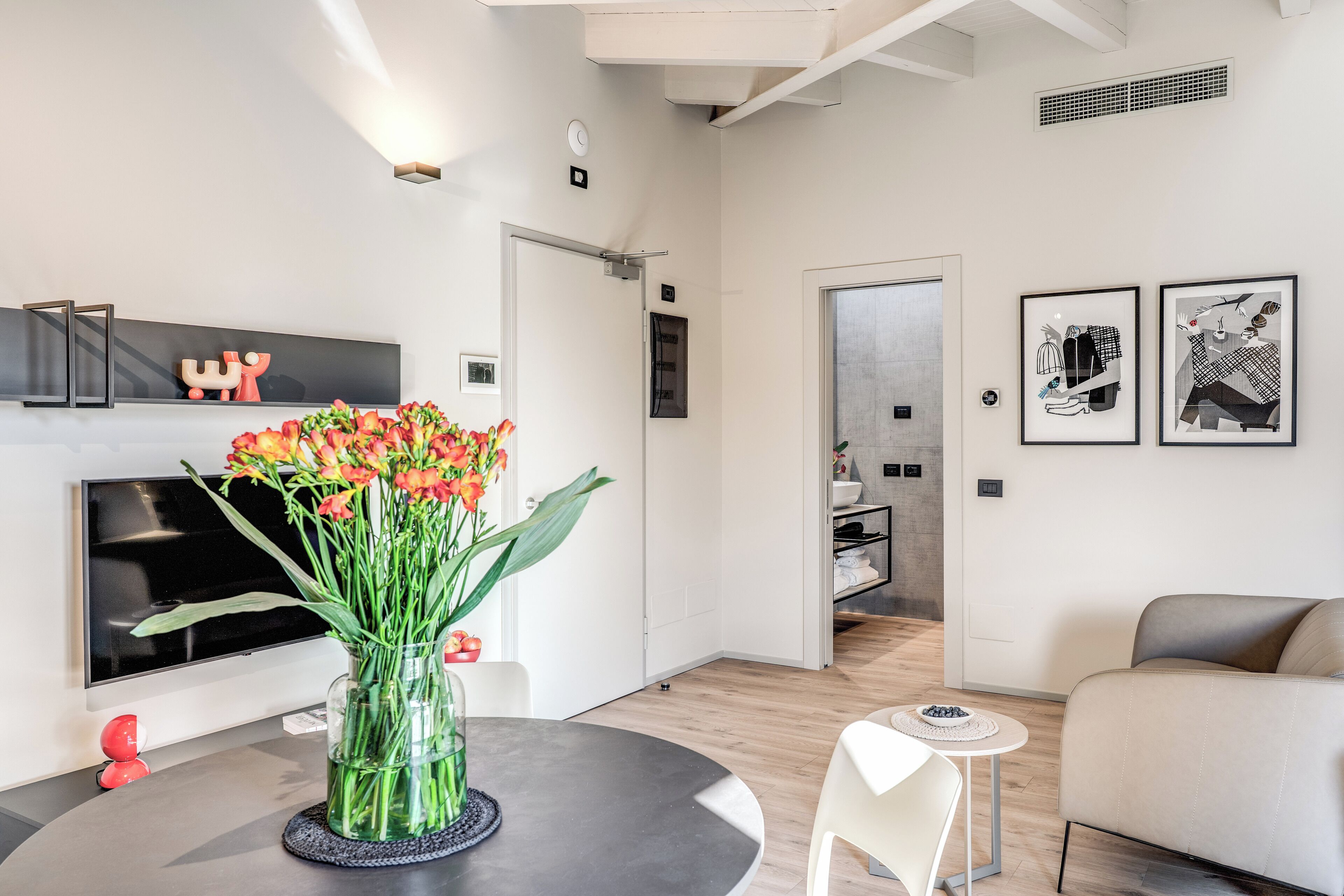 A modern living room with a round table, a vase of flowers, a sofa, and artwork on the walls.
