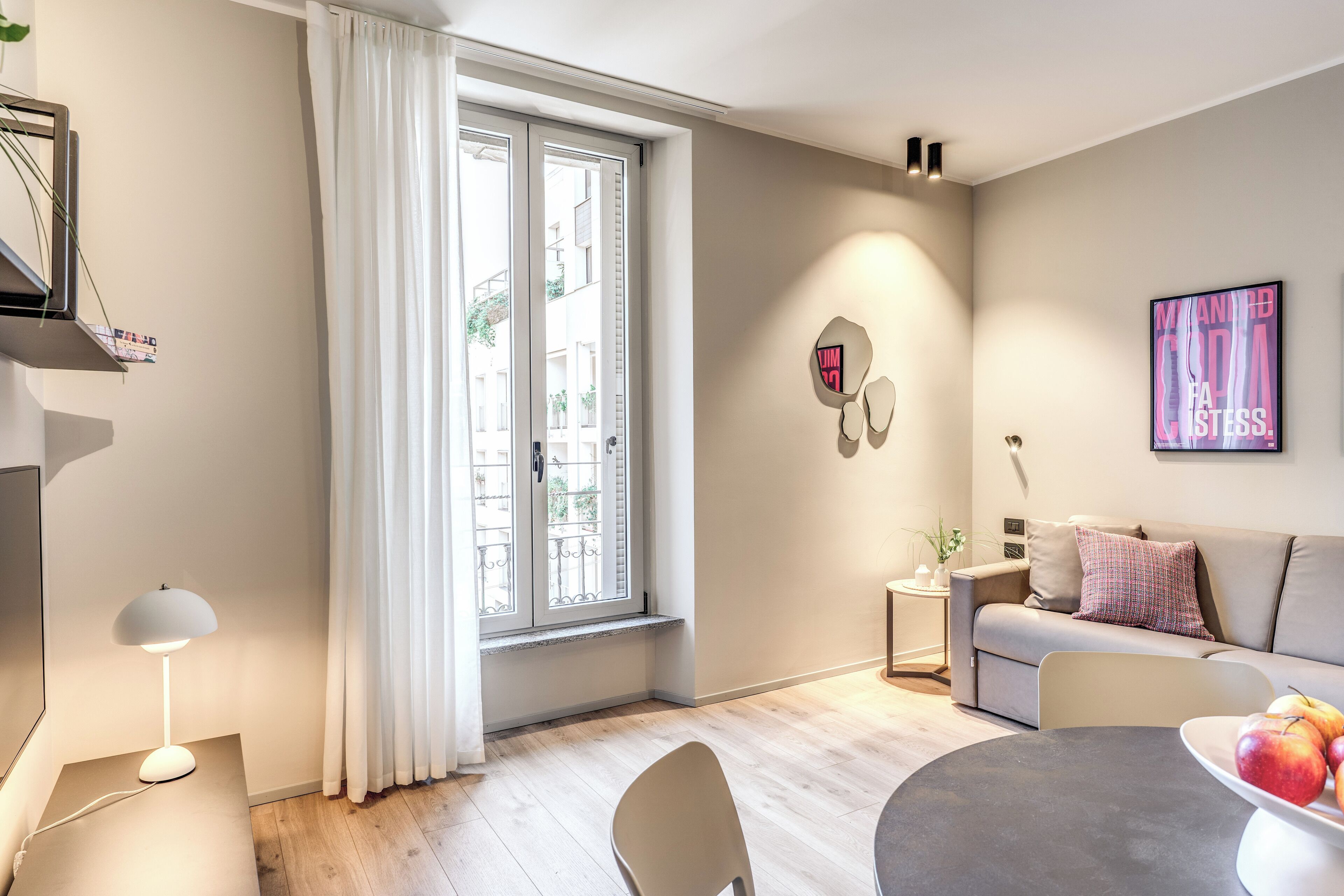Ein modernes Wohnzimmer mit einer Couch, einem Esstisch mit Äpfeln, einer Lampe und einem Fenster mit Vorhängen.