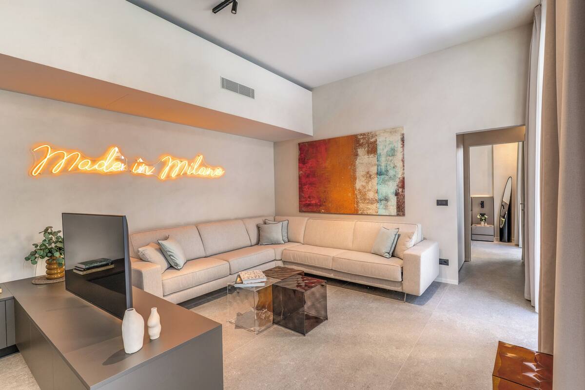 Una sala de estar moderna con un sofá seccional, un televisor de pantalla plana, una mesa de centro y un letrero de neón en la pared.
