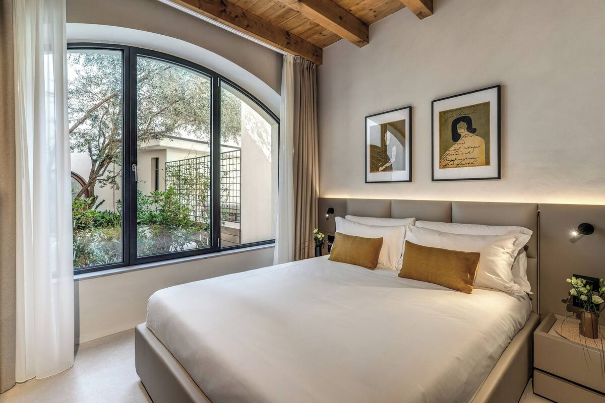 Un dormitorio con una cama grande, un ventanal curvo y dos cuadros en la pared.