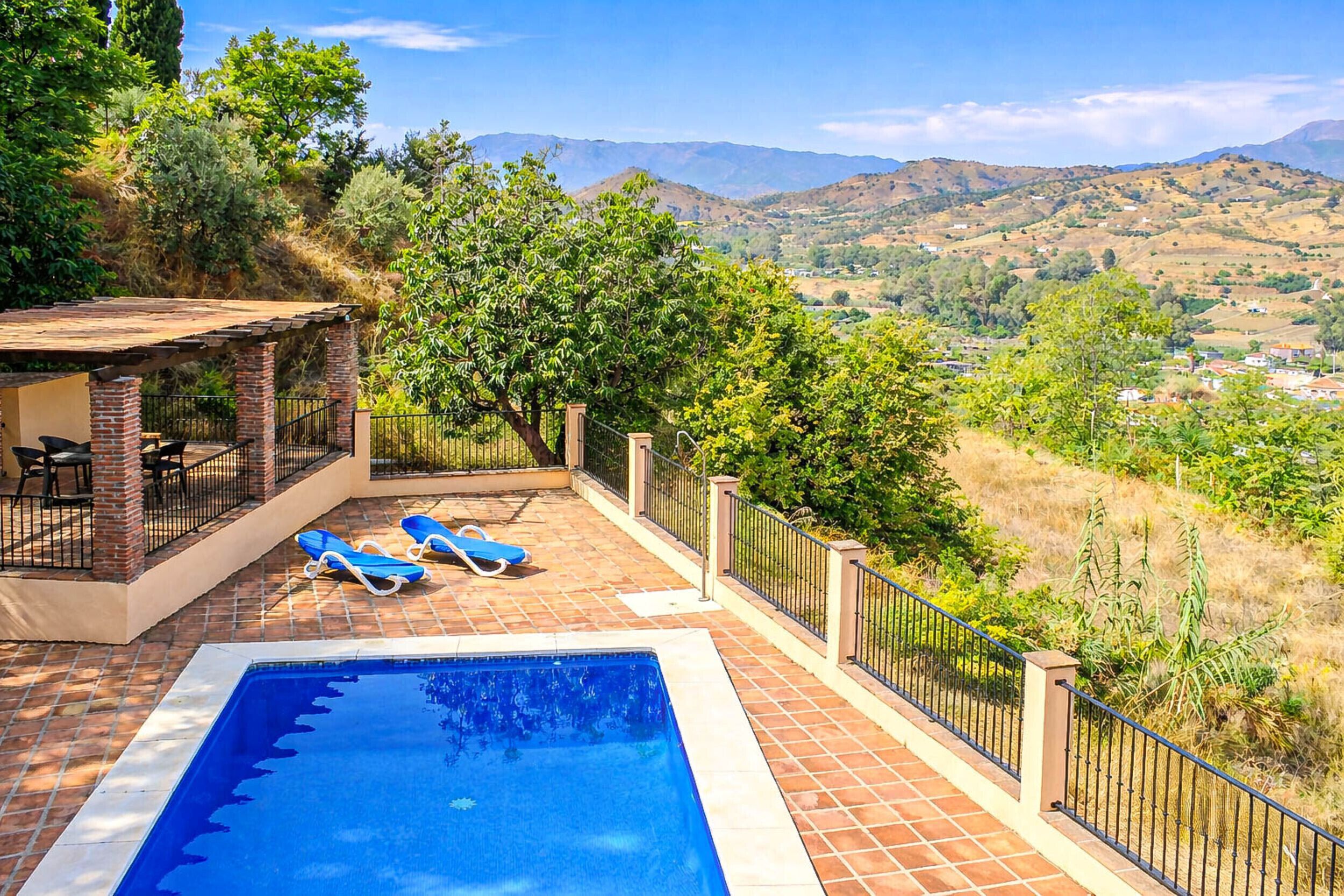 Une piscine avec deux chaises longues, un espace salon couvert et une vue sur les collines et les montagnes.