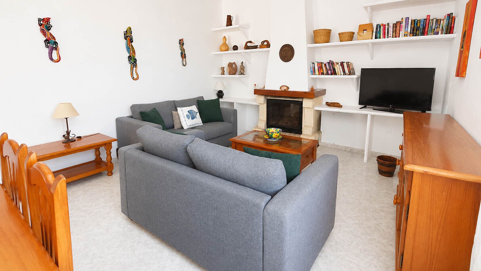 Un salon avec un canapé gris, une table basse en bois, un téléviseur, une bibliothèque et des objets de décoration.