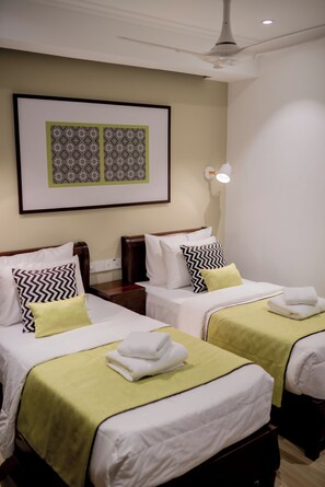 Ein Hotelzimmer mit zwei Einzelbetten, jeweils mit grüner Bettdecke und weißer Bettwäsche. Darüber hängt ein gerahmtes Kunstwerk, und rechts befindet sich eine Wandlampe.