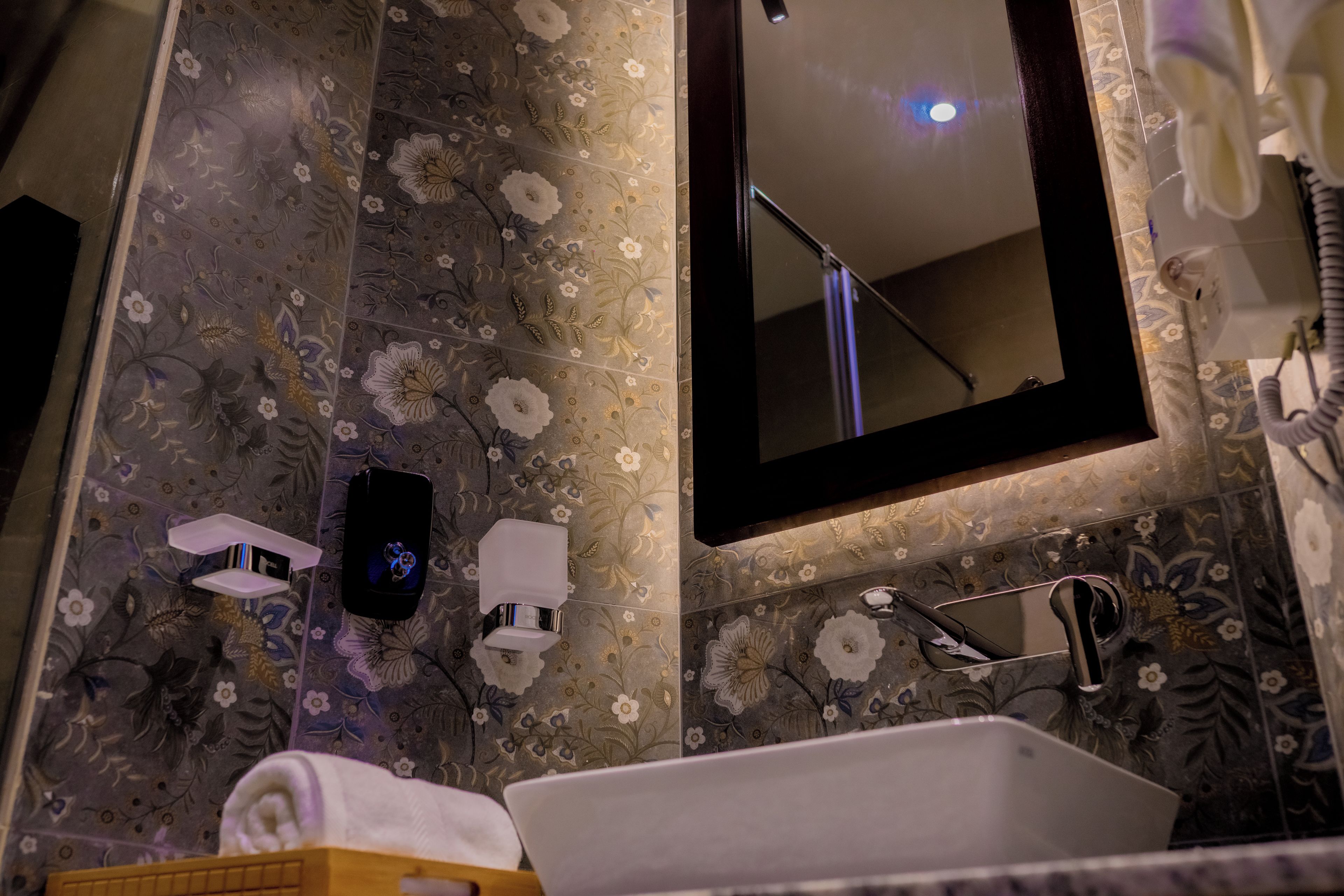 A bathroom with a sink, mirror, and floral-patterned tiles.