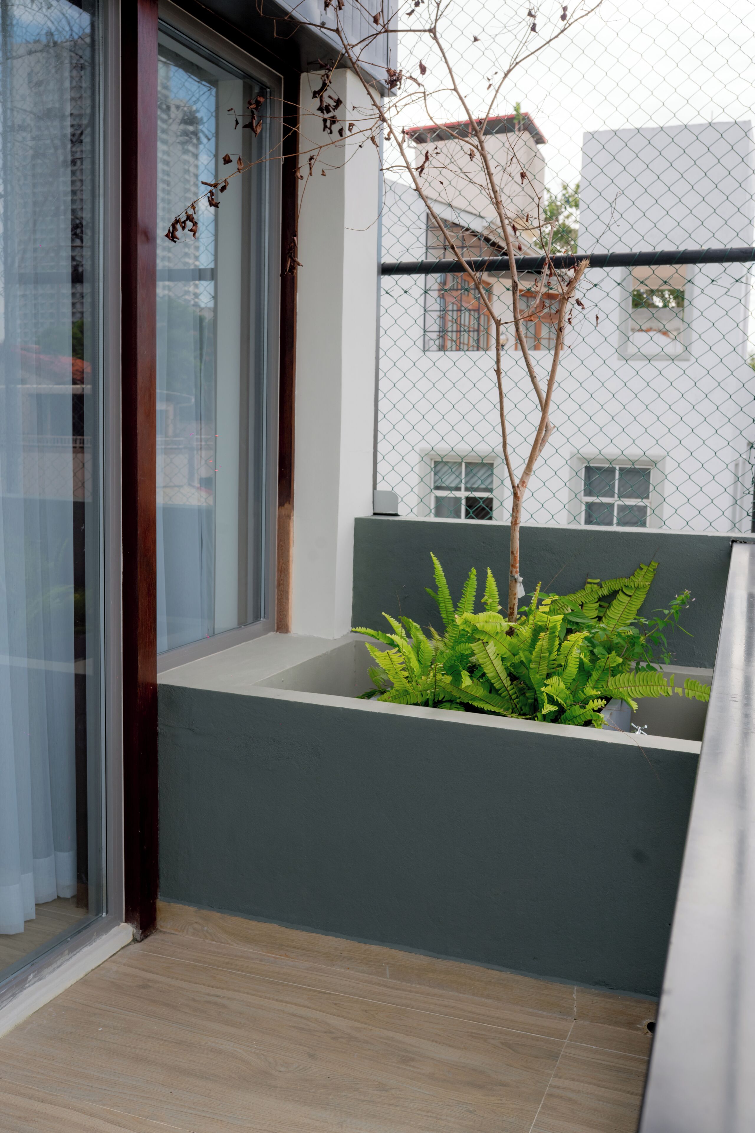Un balcón moderno con puerta de vidrio, una planta pequeña y vista de un edificio al fondo.