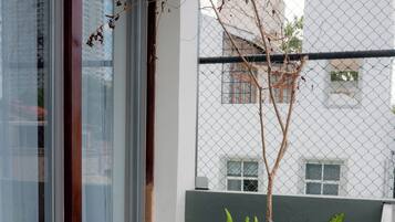 Un balcón moderno con puerta de vidrio, una planta pequeña y vista de un edificio al fondo.