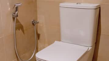 A white toilet with a shower attachment in a bathroom with beige tiles.