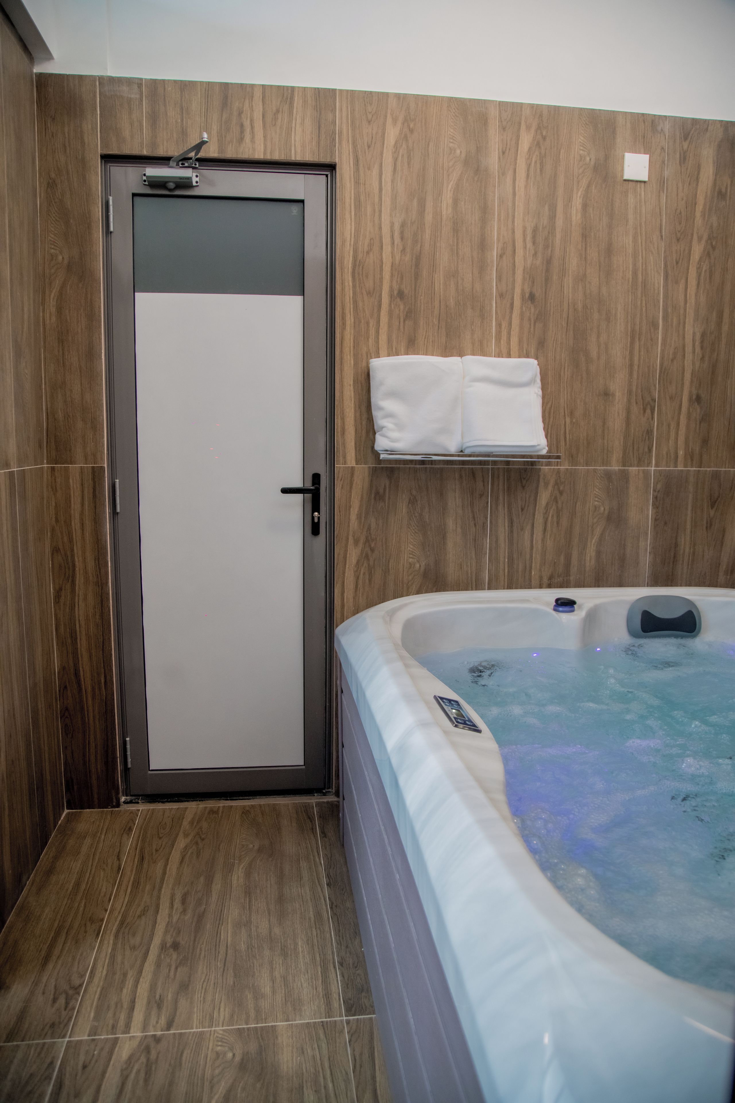 Un baño con pared de madera, puerta de cristal, bañera de hidromasaje y perchero.