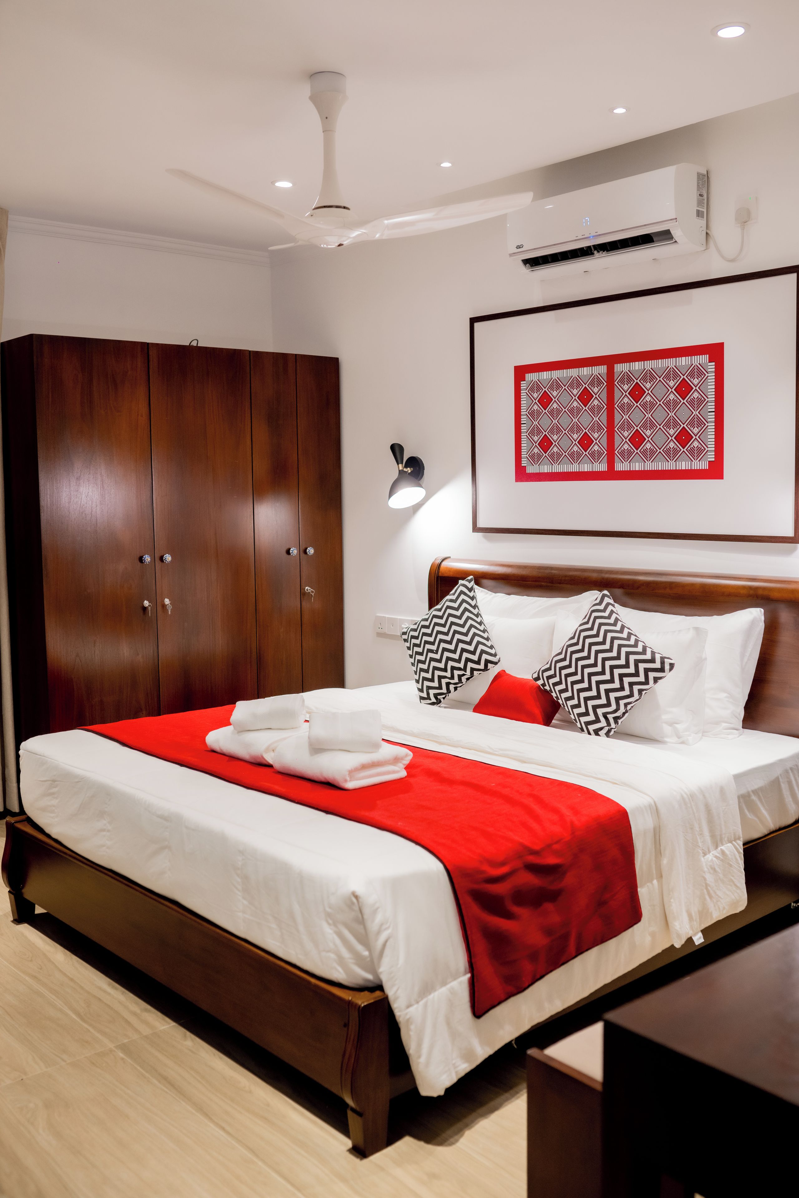 Una cama bien hecha con colcha roja y blanca, un armario de madera y un cuadro enmarcado en la pared.