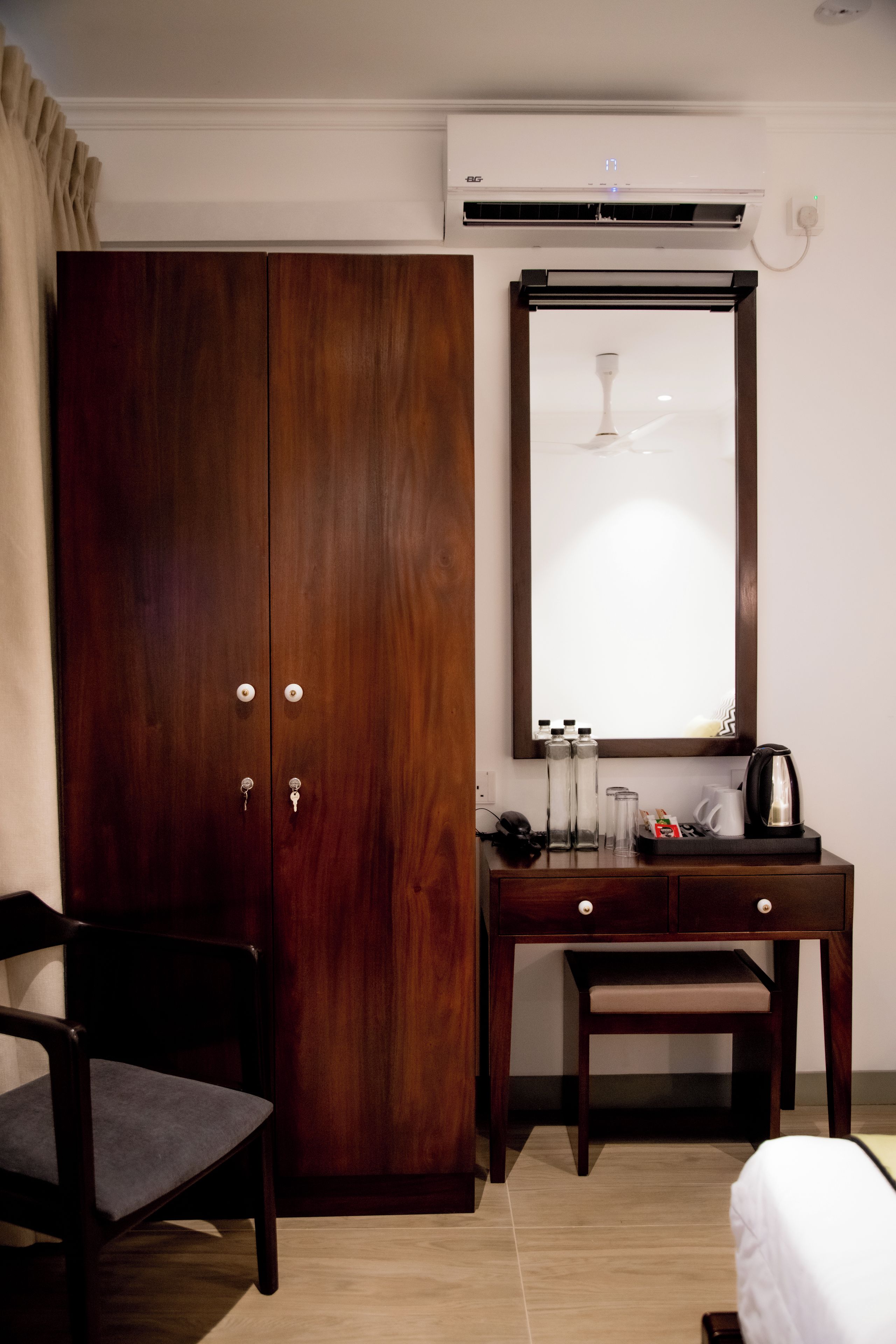 Ein Hotelzimmer mit einem Holzschrank, einem Schreibtisch mit Spiegel, einem Sessel, einem Bett und einer Kaffeemaschine.