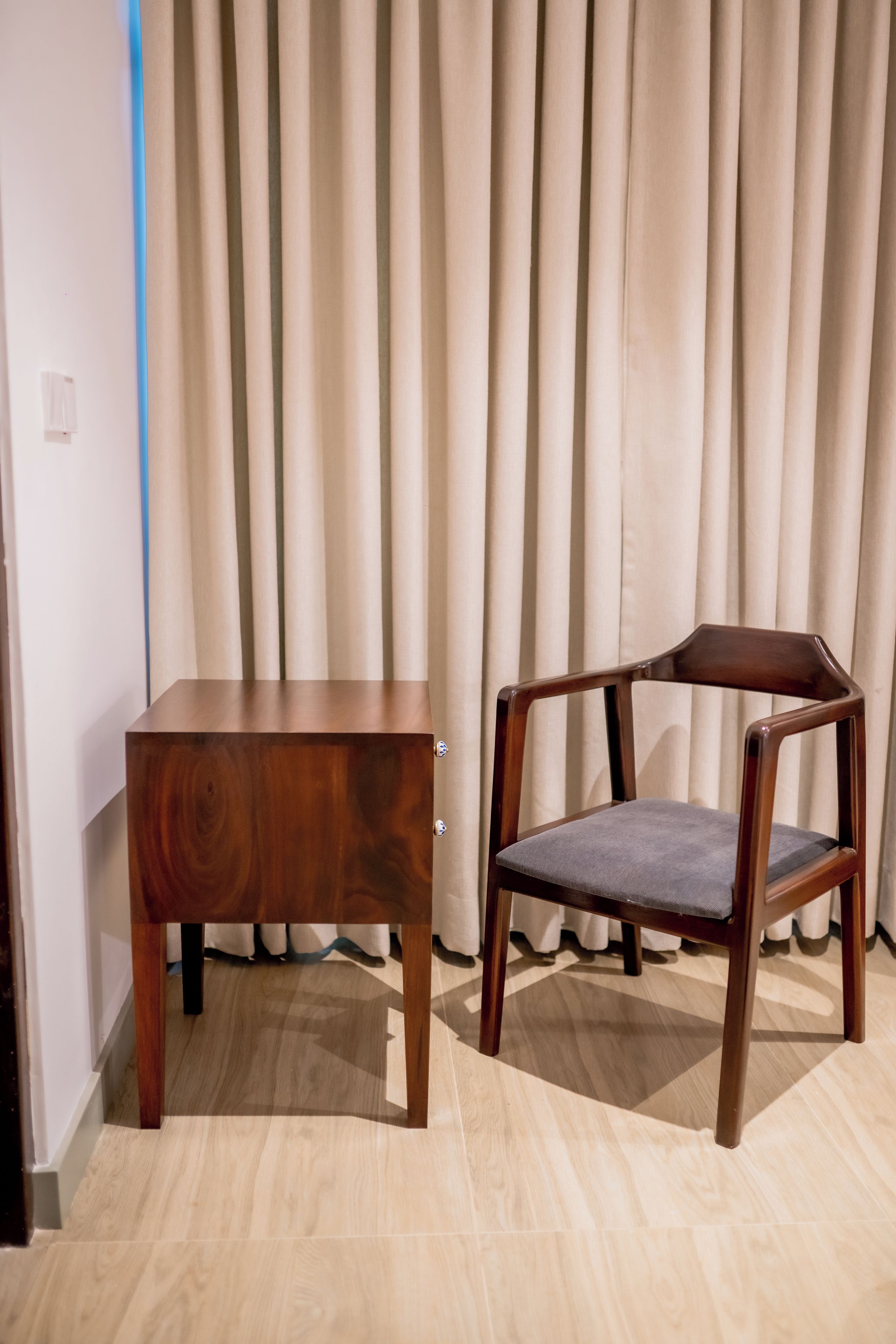 A wooden chair and a matching wooden table in a room with light-colored curtains and wooden flooring.
