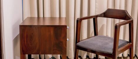 A wooden chair and a matching wooden table in a room with light-colored curtains and wooden flooring.