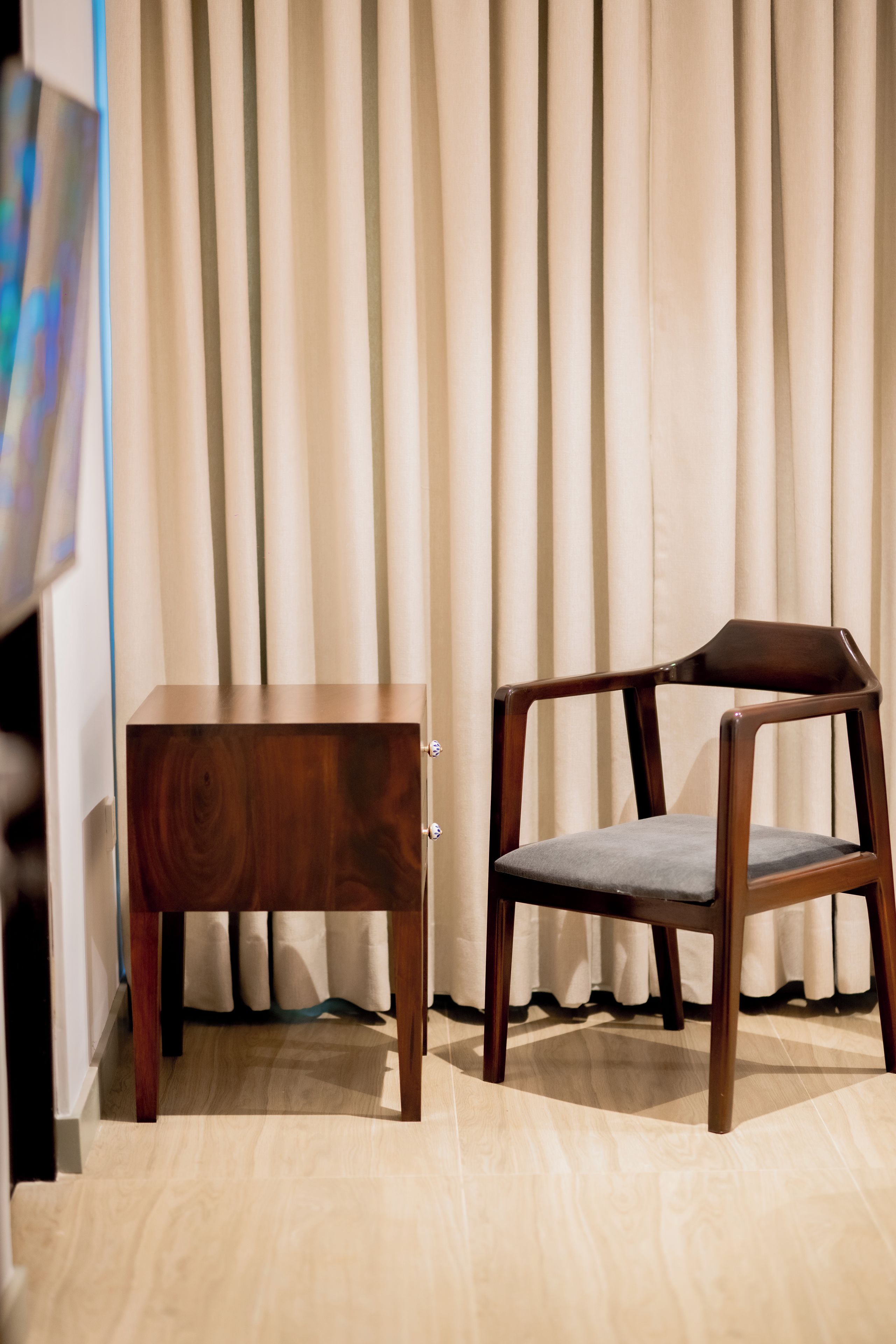 Une petite table d’appoint et une chaise en bois, dans une pièce équipée de stores verticaux.