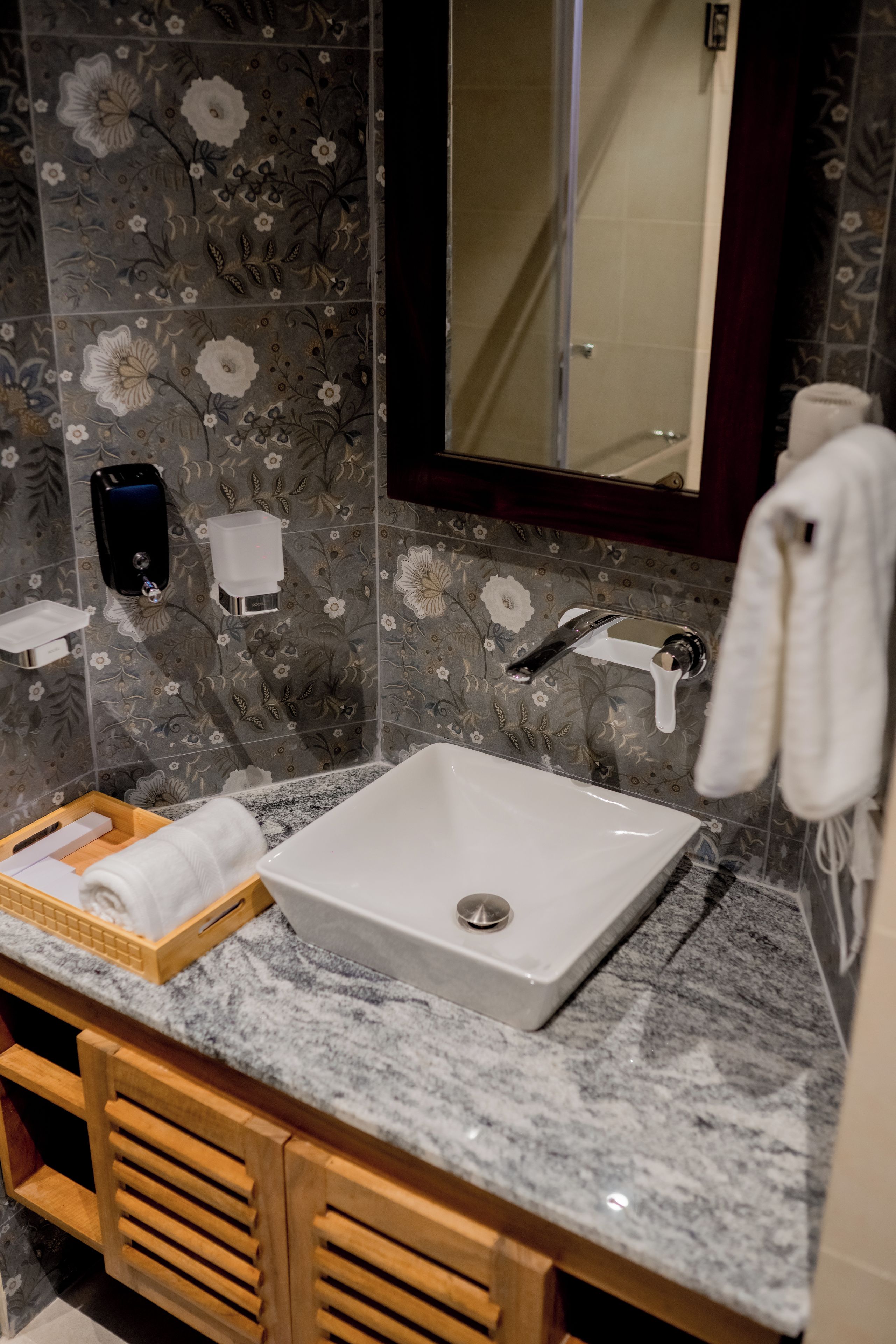 Une salle de bain avec un lavabo blanc, un miroir, un porte-serviettes et un distributeur de savon.