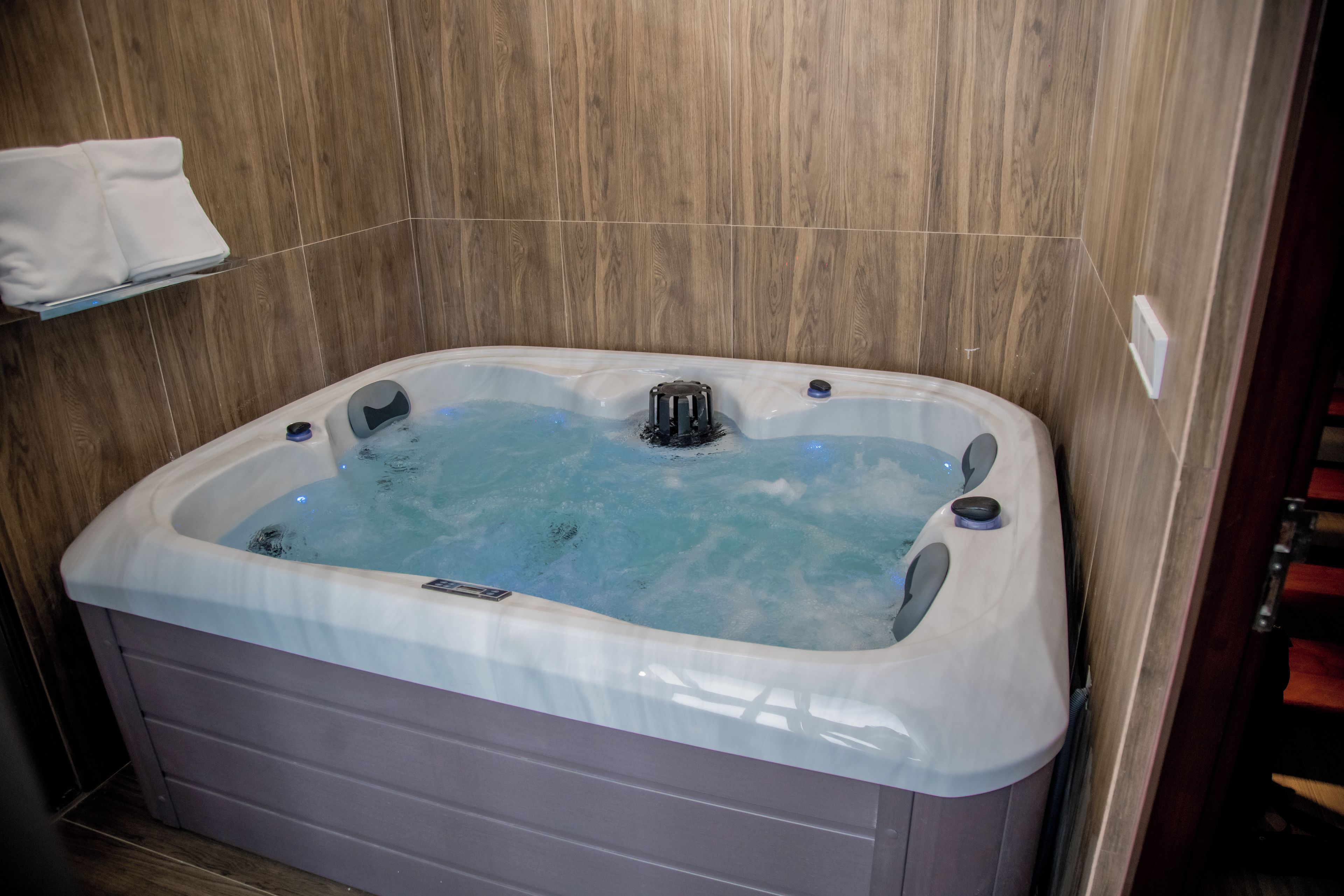 A modern bathroom with a wooden wall, a white bathtub with a built-in heater, and a towel rack above it.