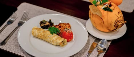 A plate with a rolled omelette, a grilled chicken breast, and a grilled tomato, accompanied by a bread roll with a decorative topping.