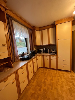 Cozinha compacta com armários de madeira, micro-ondas, cafeteira e janela com cortinas.