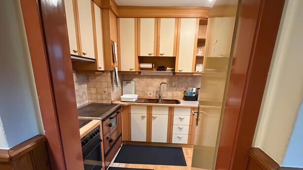 Una cocina con armarios de madera, estufa, lavaplatos y un tapete negro.