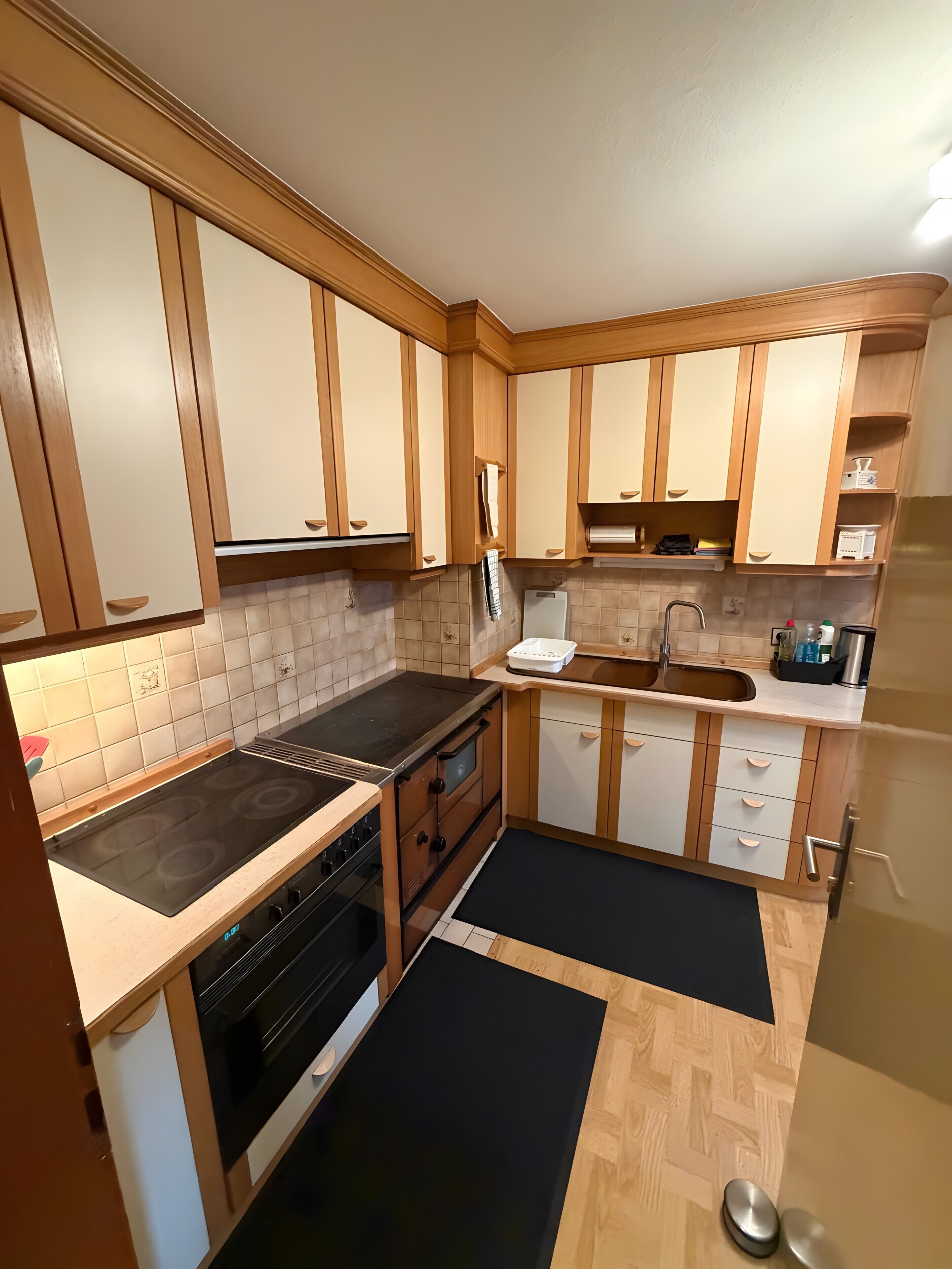 A kitchen with wooden cabinets, a stove, oven, sink, and a black rug.