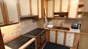 A kitchen with wooden cabinets, a stove, oven, sink, and a black rug.