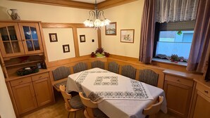 Comedor con una mesa dispuesta para cuatro, armarios de madera, una araña y una ventana con cortinas.