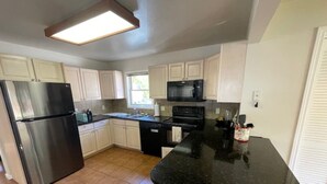 Una cocina con armarios blancos, un refrigerador de acero inoxidable, un microondas negro y una encimera negra.