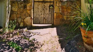 Un cancello rustico in pietra con una porta in legno, circondato da un muro in pietra e un albero.