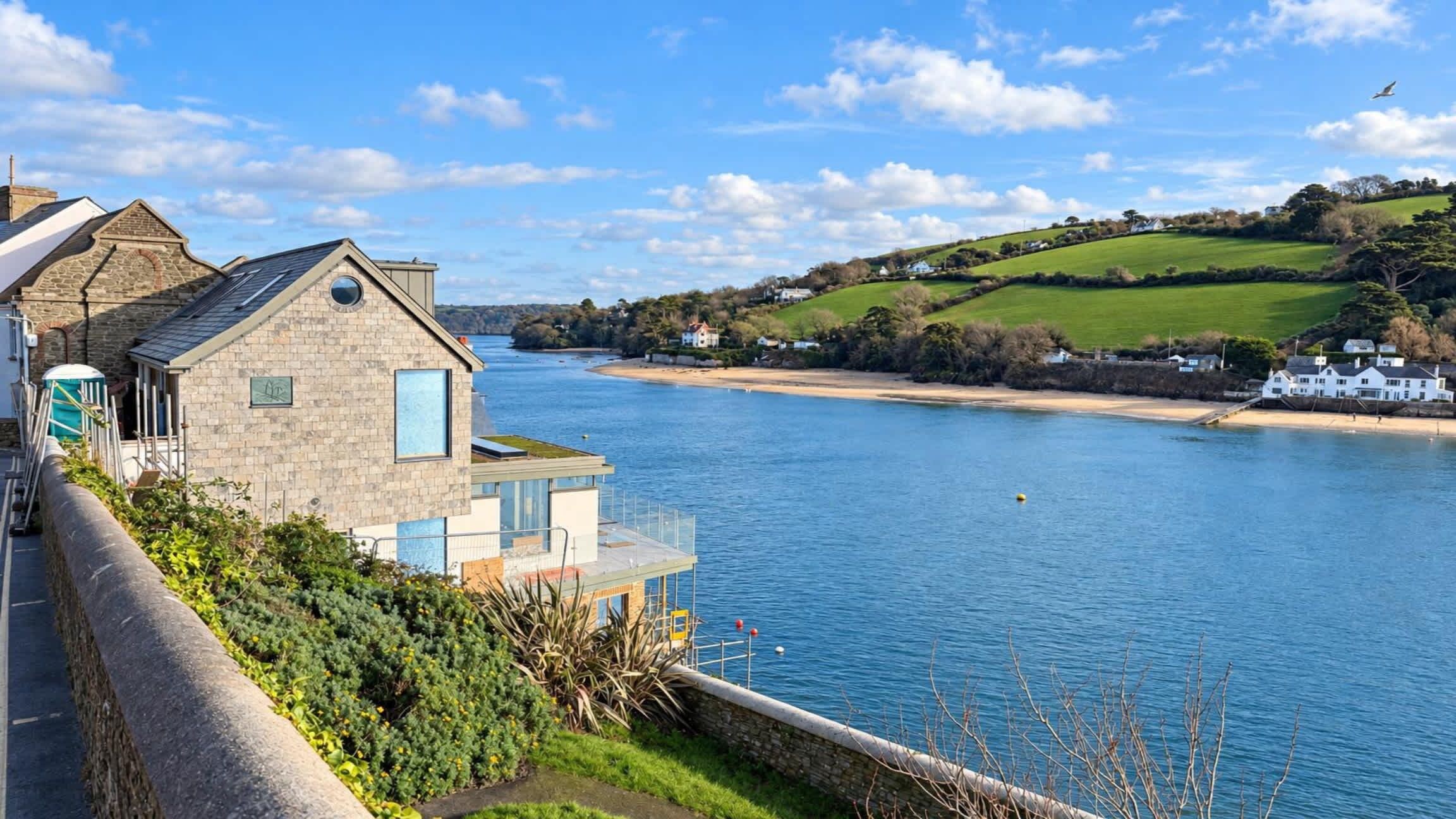 A riverside property with a stone building, a dock, and a view of the water and hills.