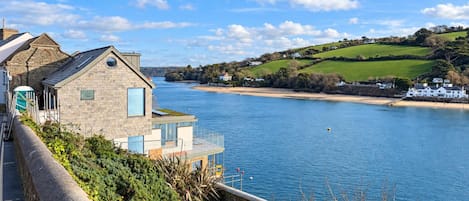 A riverside property with a stone building, a dock, and a view of the water and hills.