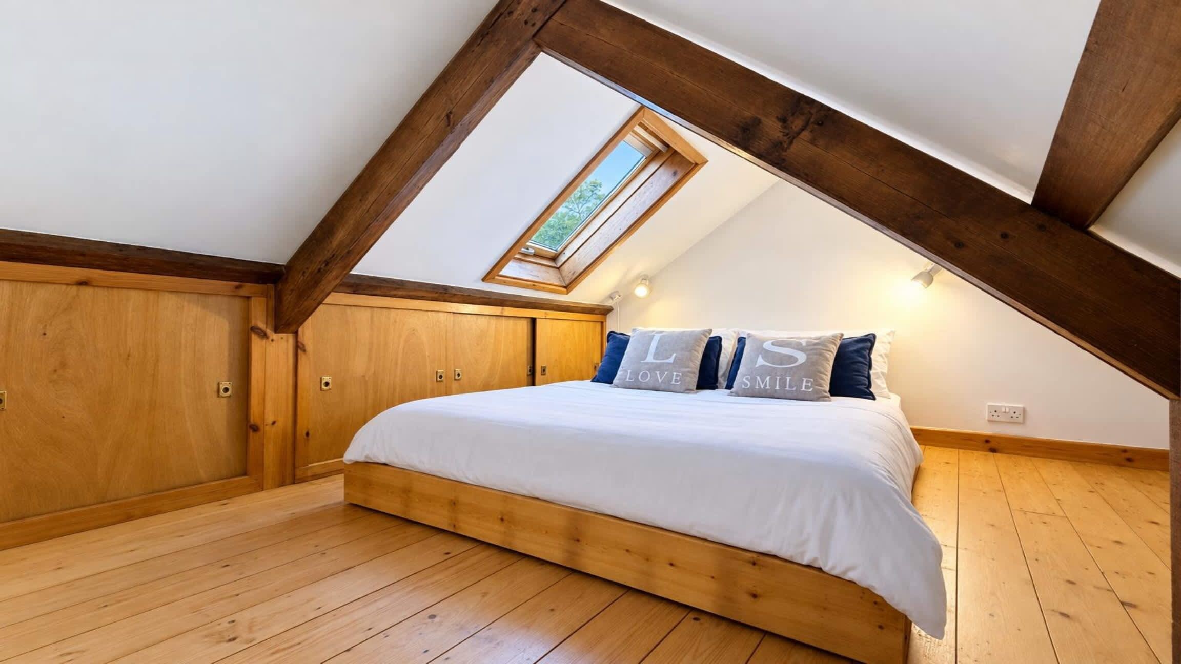 A bedroom with a sloped ceiling, wooden flooring, a bed with white bedding, and a skylight.