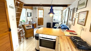 A compact kitchen with a wooden countertop, a built-in oven, and a dining area with a chair and table. - The Cabin - Hidden Retreat in the Heart of Salcombe (Salcombe)