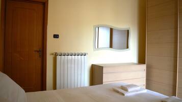 Una camera d'albergo con una porta in legno, un termosifone, uno specchio, un comò in legno e un letto rifatto con cura.