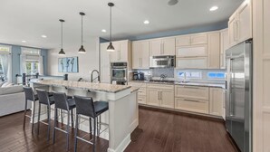 Een moderne keuken met een centraal eiland, barkrukken, roestvrijstalen apparatuur en hanglampen.