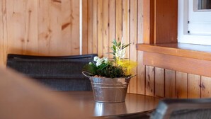 A metal bucket with a plant on a wooden table in a room with wooden walls and a window.