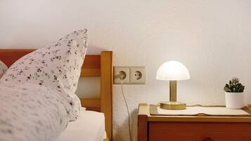 Un letto rifatto con biancheria da letto floreale, una lampada da comodino, un piccolo comodino in legno e una pianta in vaso.