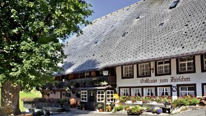 Um edifício tradicional com telhado de telhas, várias janelas e uma placa com a inscrição 'Gathaus zum Hirschchen'.