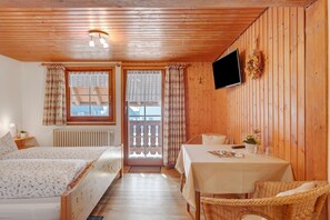 Una habitación con paneles de madera, dos camas, una mesa, sillas de mimbre, un televisor y una ventana con cortinas.
