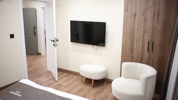 Un dormitorio con una cama, un televisor montado en la pared, un armario de madera y un sillón blanco.