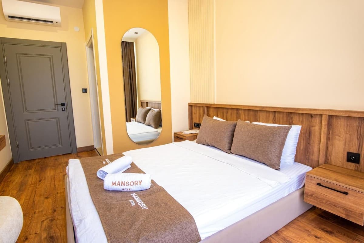 A hotel room with a large bed, a wooden headboard, a bedside table, a mirror, and a door.