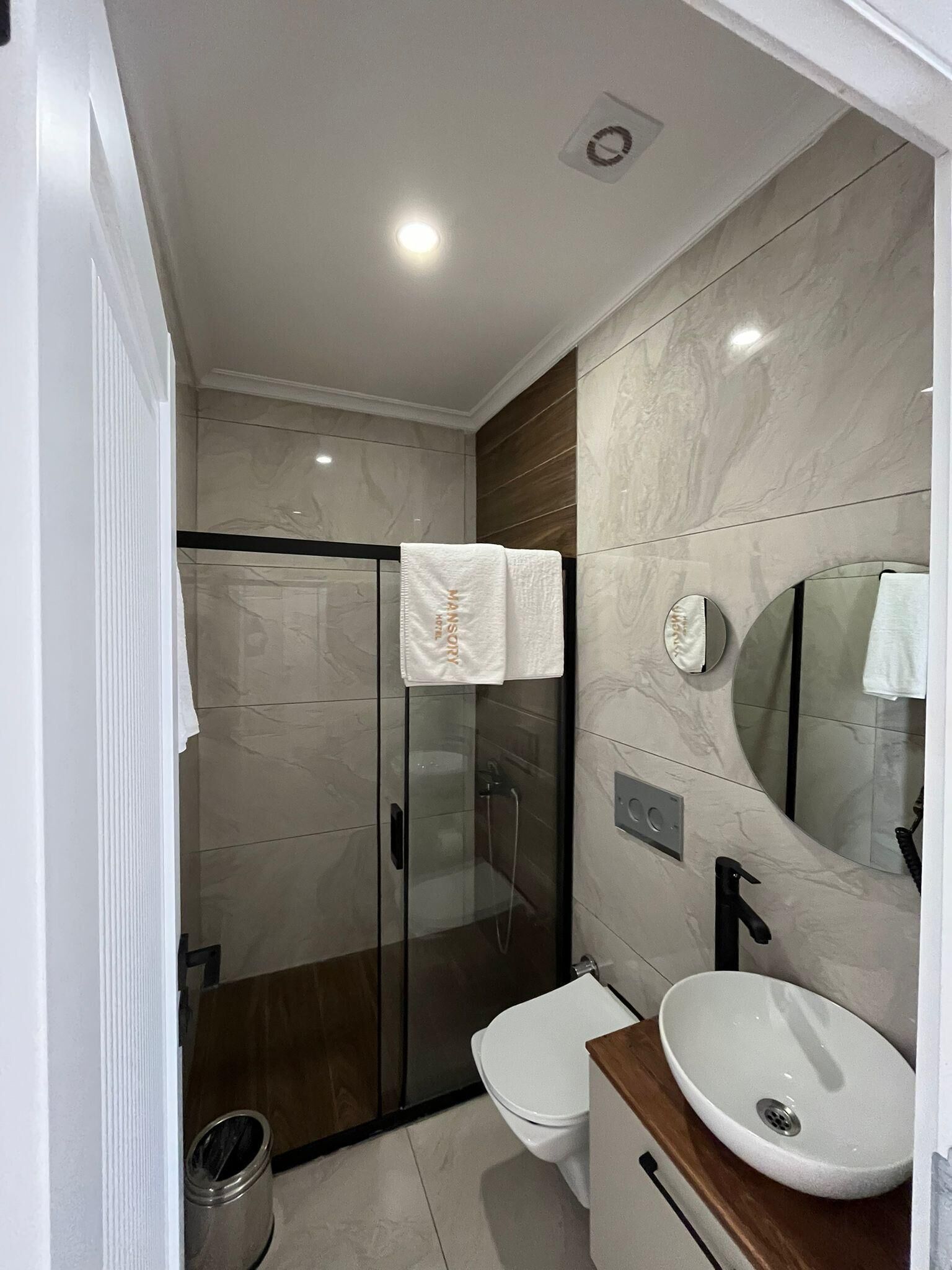 Un baño moderno con ducha de vidrio, inodoro y lavamanos con encimera de madera.